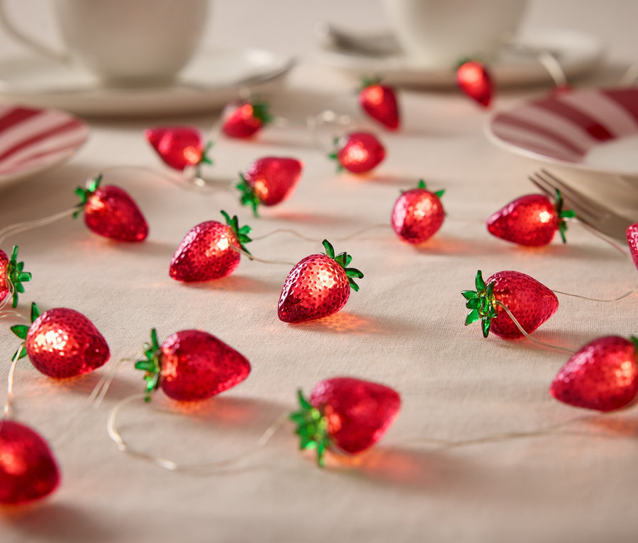 Svetelná reťaz v tvare jahôd na stole s riadom.