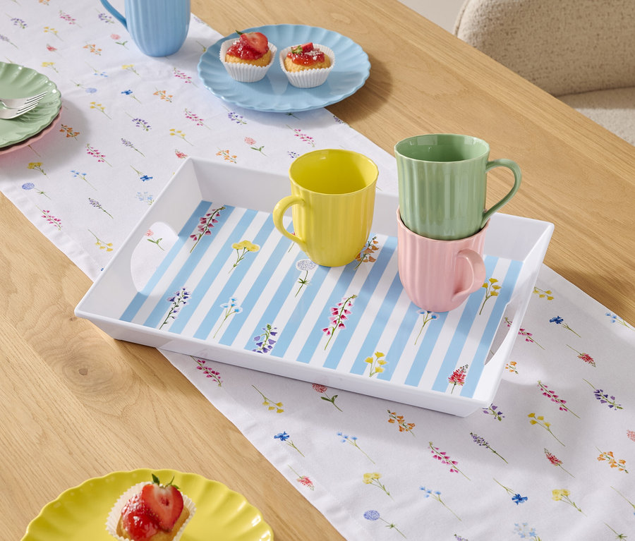 Jedálenský stôl s riadom a šálkami na kvetinovom obruse.