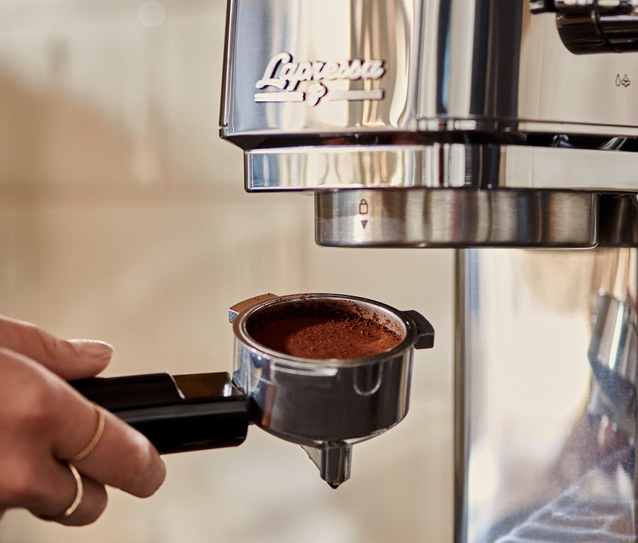 Žena vkladá strieborný pákový kávovar »Lapressa« s kávou do kávovaru.