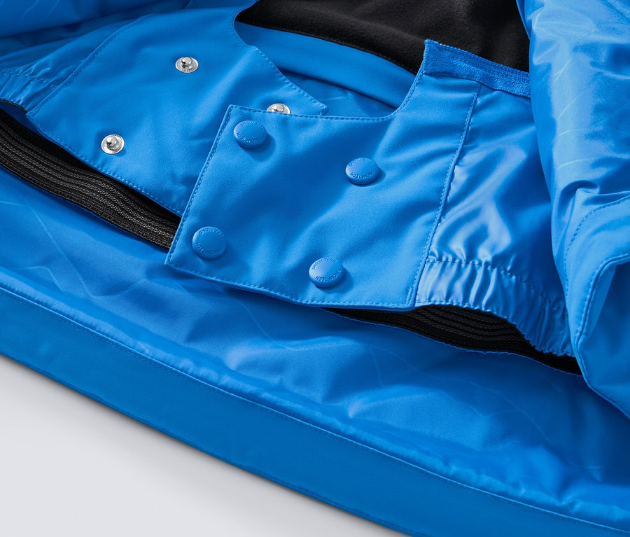 Detail modrej high-tech lyžiarskej bundy s gombíkmi a čiernym lemom.