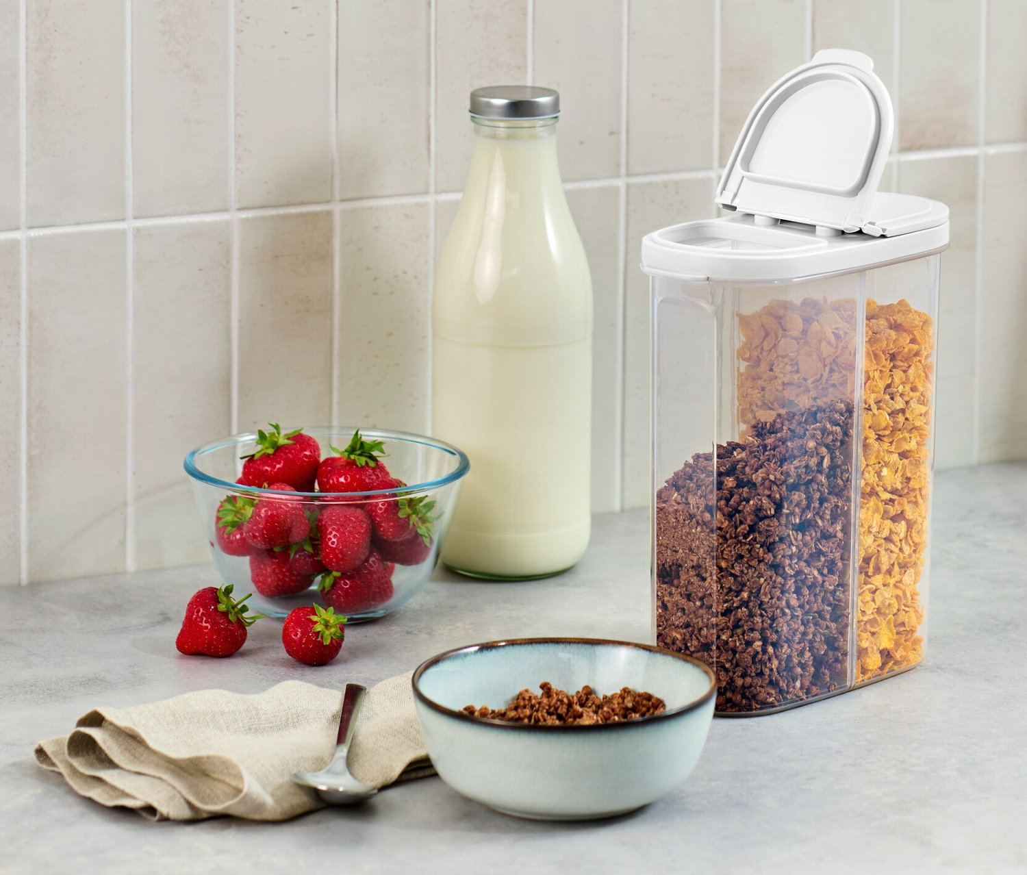 Na linke stojí dóza na potraviny 2 v 1, miska jahôd, fľaša mlieka a miska cereálií.