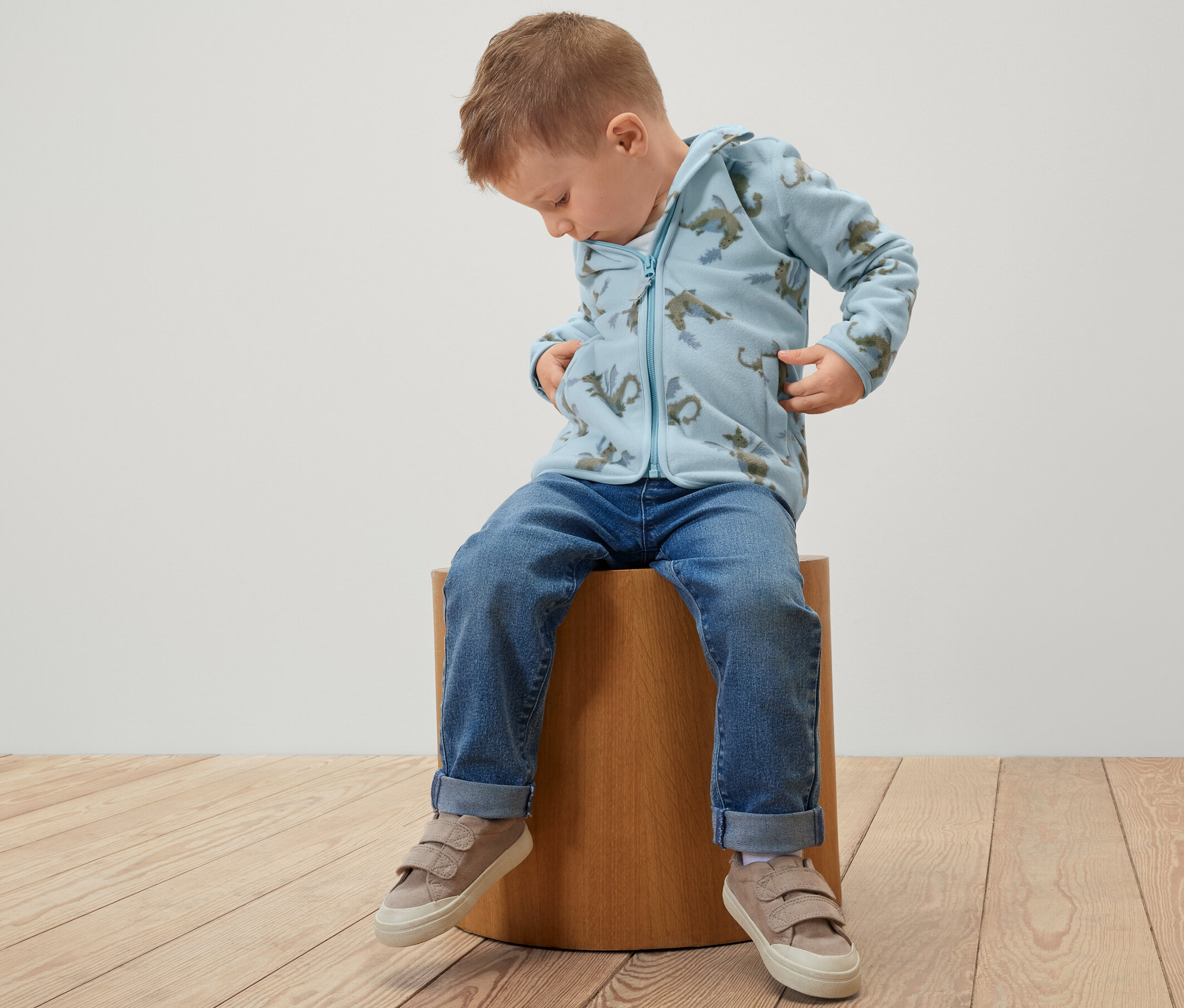 Chlapec sedí na stoličke a má na sebe detskú flaušovú mikinu s drakom.