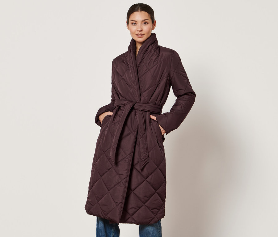 Žena pózuje v prešívanom kabáte.