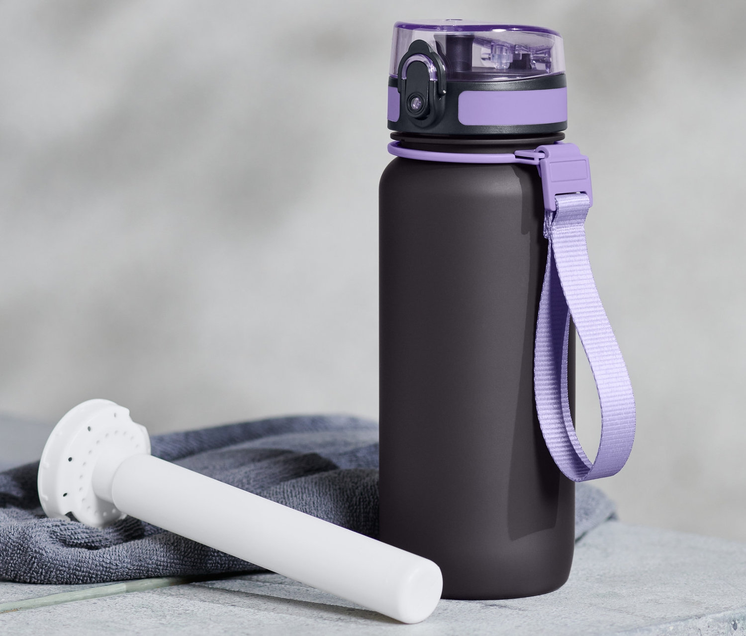 Čierna fľaša na pitie s fialovými detailmi a bielym chladiacim prvkom leží na sivom povrchu.