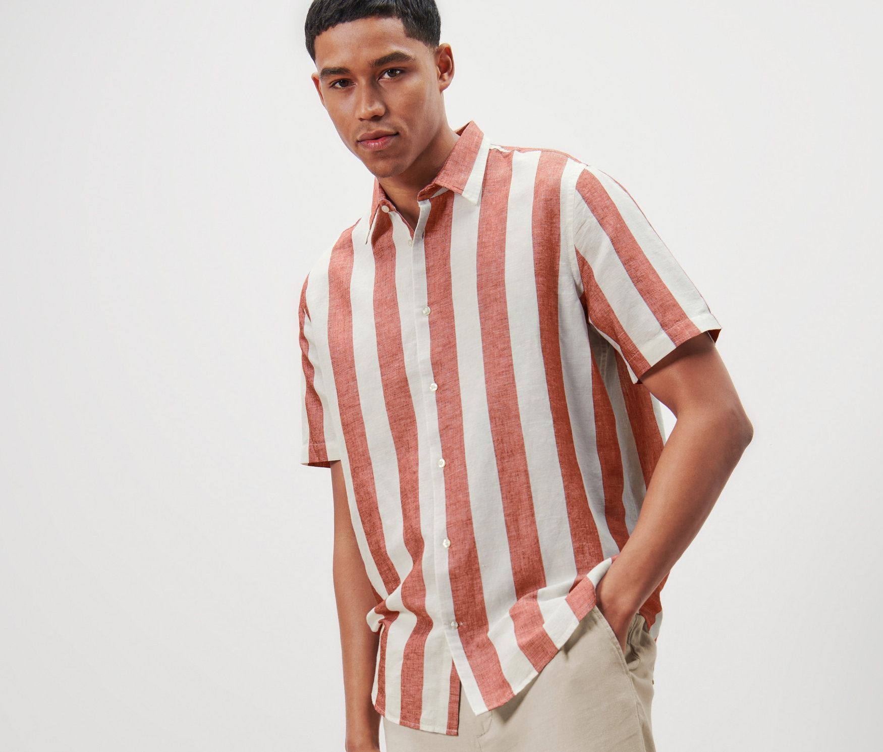 Muž pózuje v pruhovanej košeli s krátkymi rukávmi, s ľanom a svetlých nohaviciach.