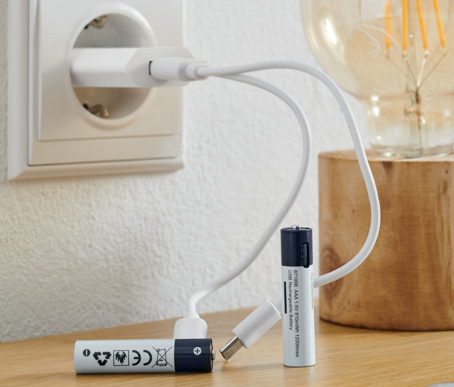 Dve nabíjacie batérie AAA ležia na stole s nabíjacím káblom zapojeným do zásuvky.