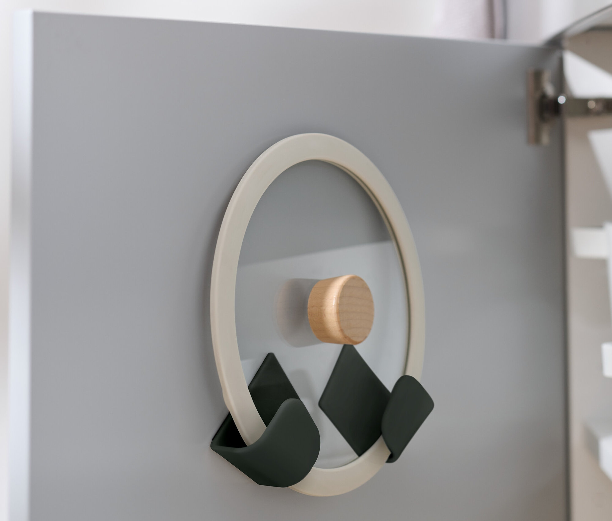 Držiak na pokrievku, 4 držiaky na stenu na pokrievky, pripevnený na vnútornej strane sivých dverí skrinky.