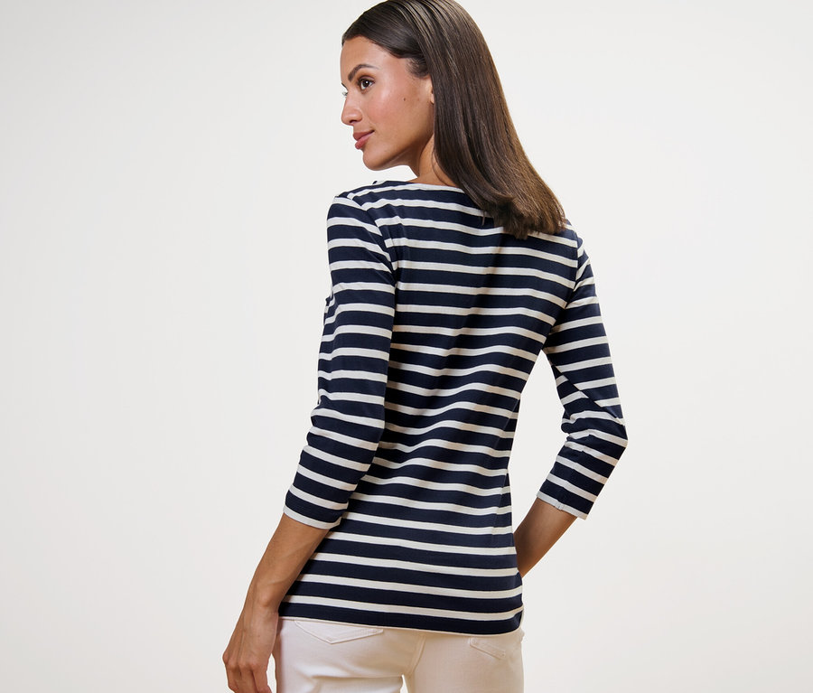 Žena má na sebe prúžkované tričko s trojštvrťovými rukávmi s prúžkami v námorníckej modrej a svetlé nohavice.