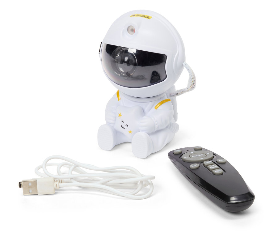 Biely projektor nočnej oblohy v tvare astronauta sedí vedľa čierneho diaľkového ovládača a bieleho USB kábla.