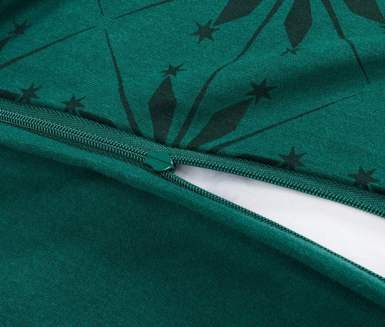Detailný pohľad na rozopnutý zips na zelenom obliečke s tmavozeleným geometrickým vzorom.