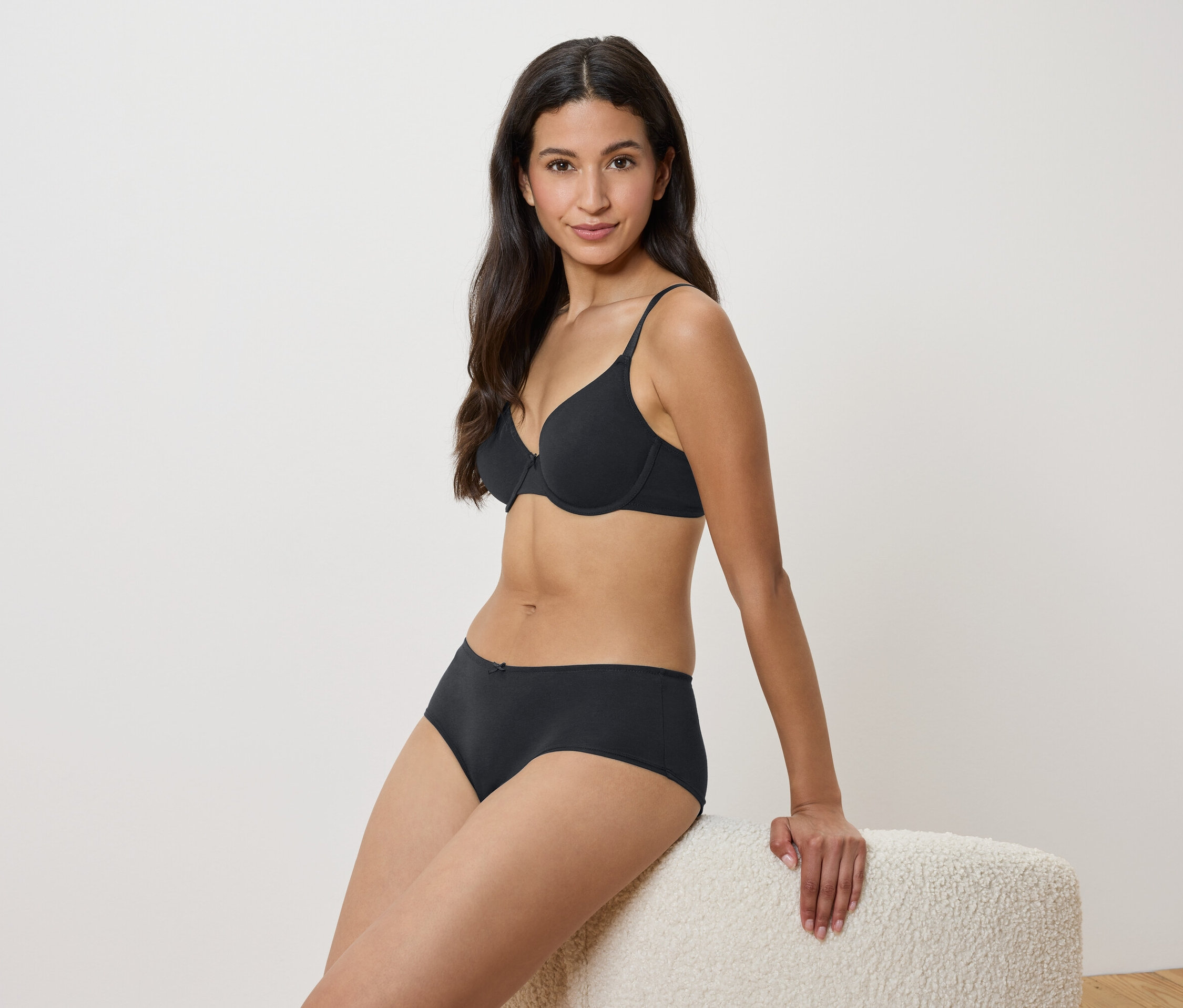 Žena sedí na taburetke v čiernej podprsenke a nohavičkách.