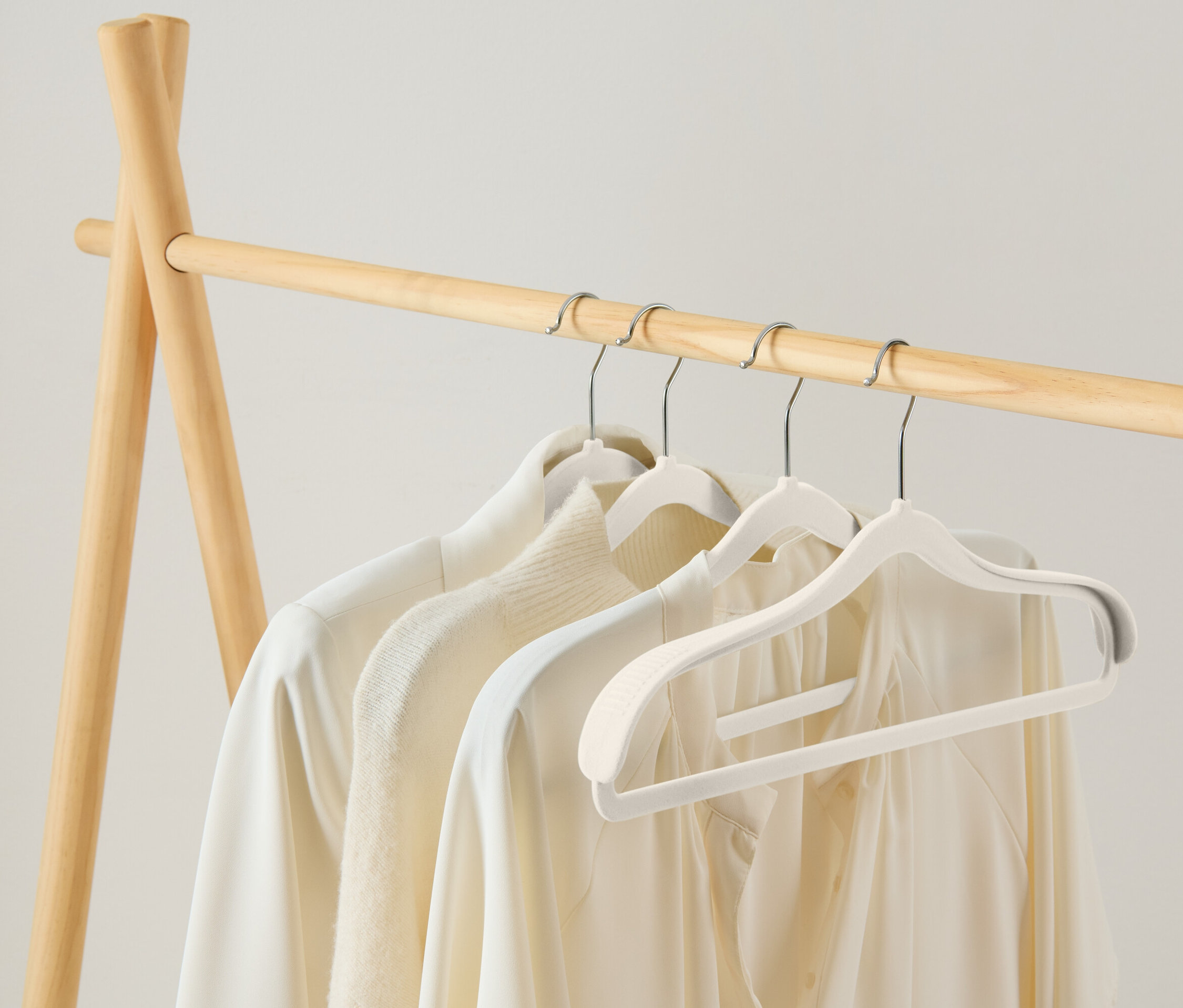 Tri biele blúzky visia na bielych vešiakoch na drevenom stojane.
