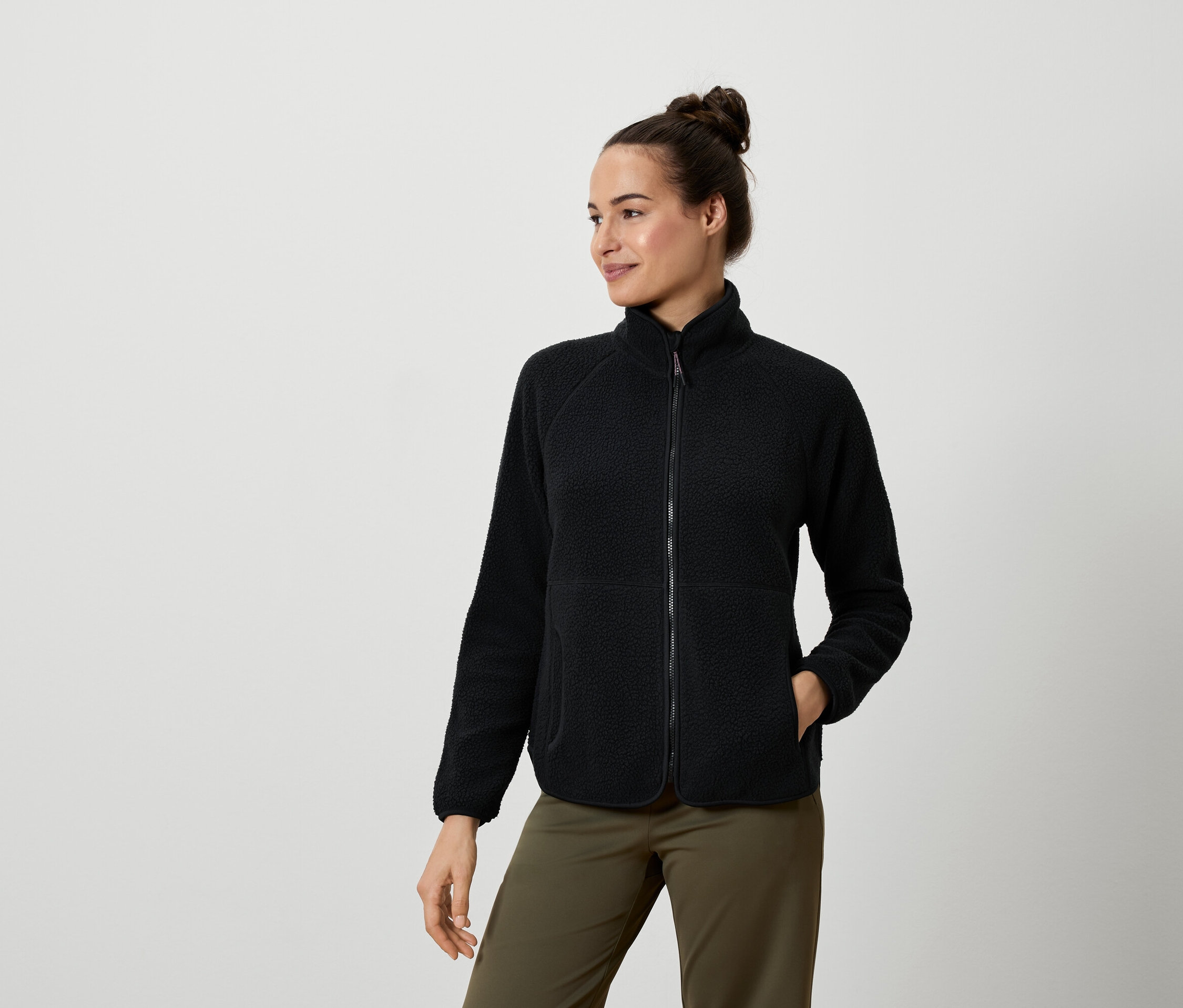 Žena má na sebe čiernu flisovú bundu a olivovozelené nohavice.