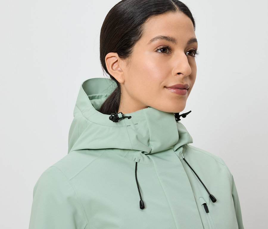 Žena má na sebe svetlozelenú bundu s kapucňou.