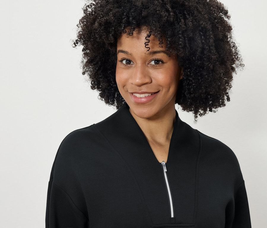 Portrét usmievajúcej sa ženy s afro účesom v čiernej mikine na zips.