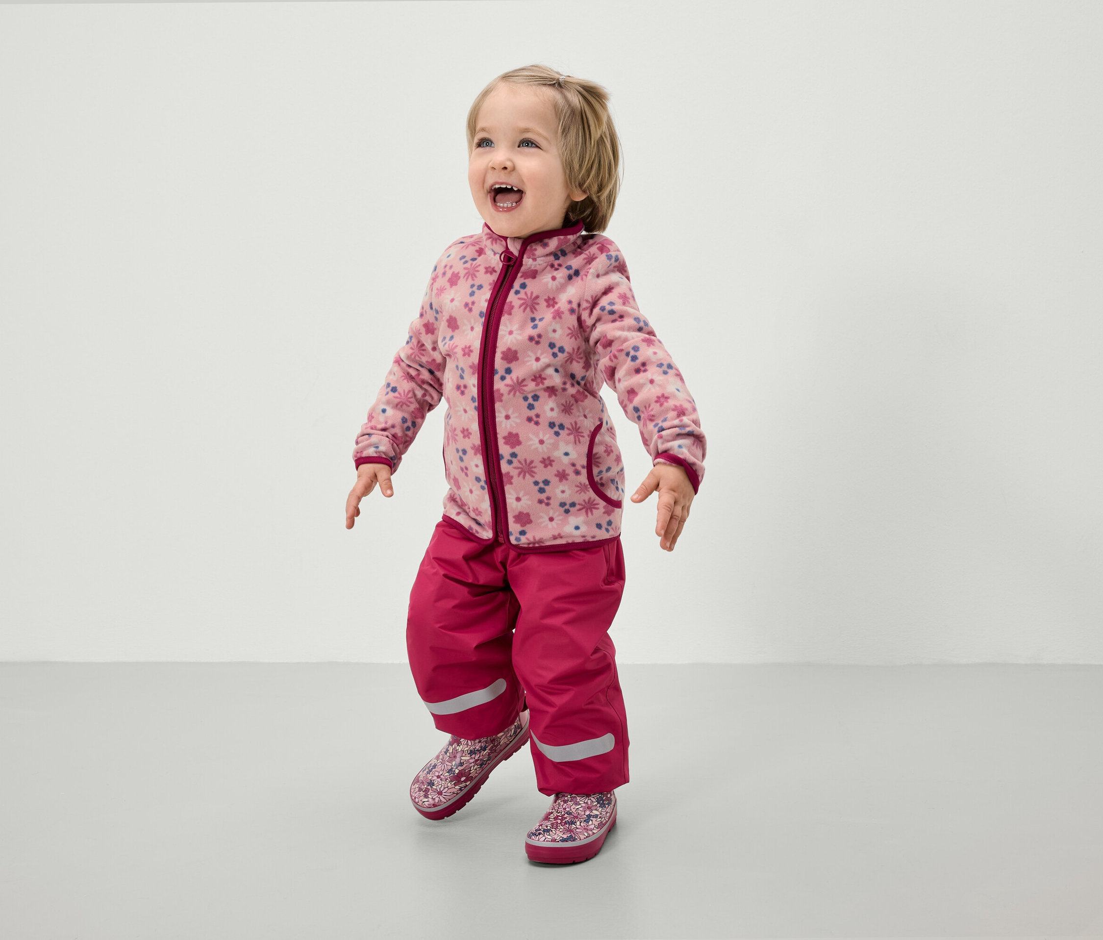 Batoľa v ružovej fleecovej bunde s kvetinovým vzorom a ružových nohaviciach.