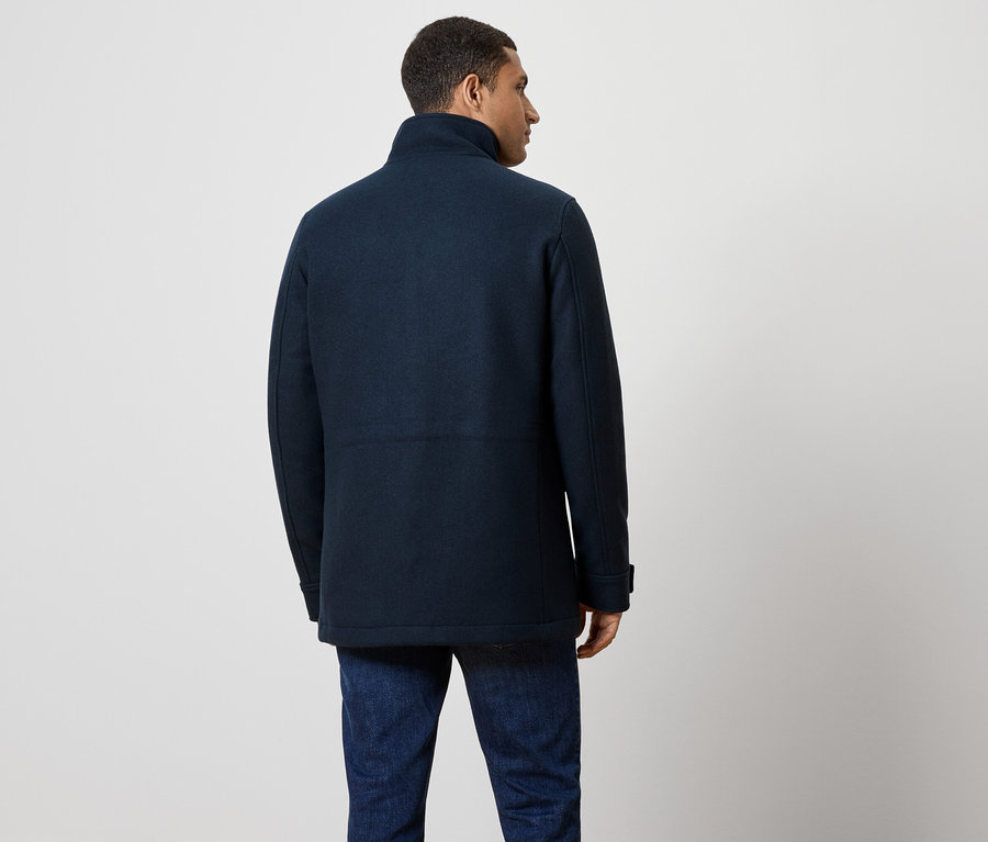 Muž chrbtom, má na sebe tmavomodrý kabát a džínsy.