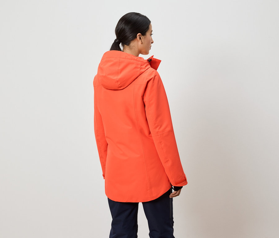 Žena chrbtom k fotoaparátu má na sebe oranžovú bundu s kapucňou.