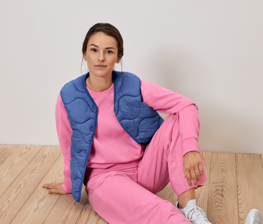 Žena sedí na podlahe v ružovej súprave a modrej veste.