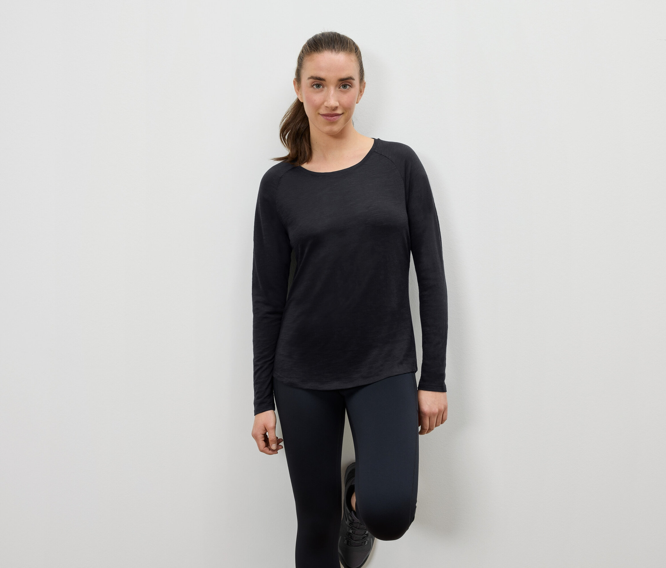 Žena v čiernom športovom oblečení opretá o stenu.