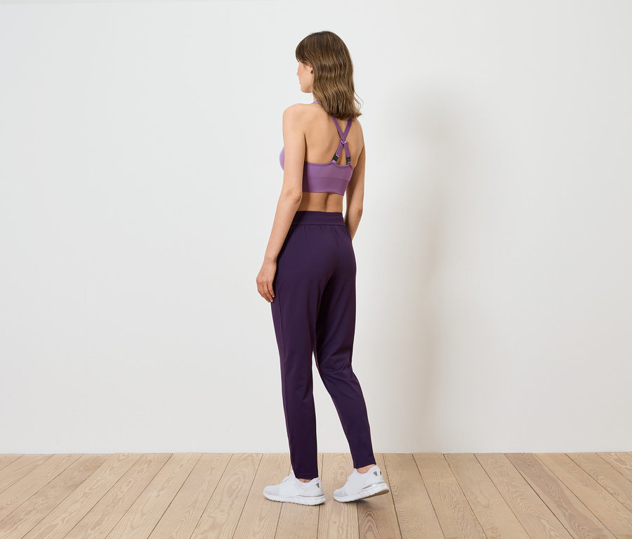 Žena zobrazená zozadu má na sebe fialovú športovú podprsenku a tmavofialové nohavice.