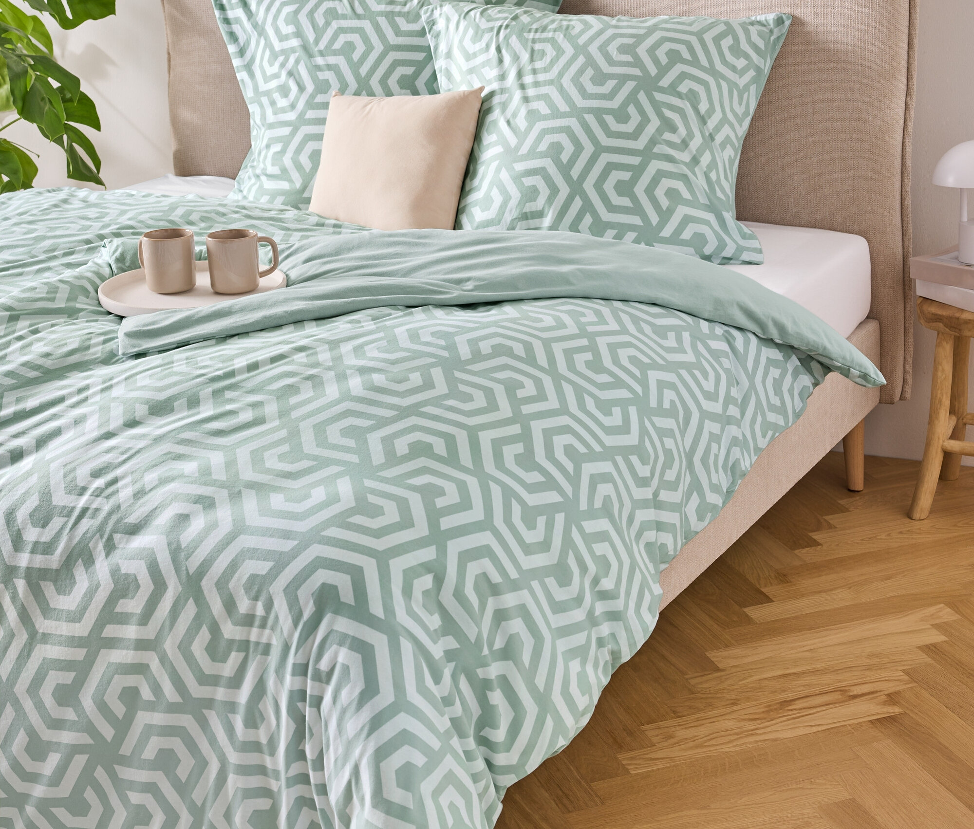 Posteľ s bledomodro-bielou pruhovanou posteľnou bielizňou, dvoma vankúšmi a podnosom s dvoma šálkami.