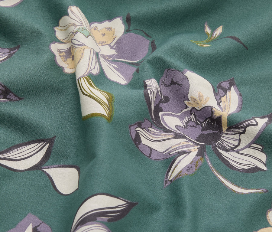 Detail látky s kvetinovým vzorom v odtieňoch zelenej, fialovej a krémovej.