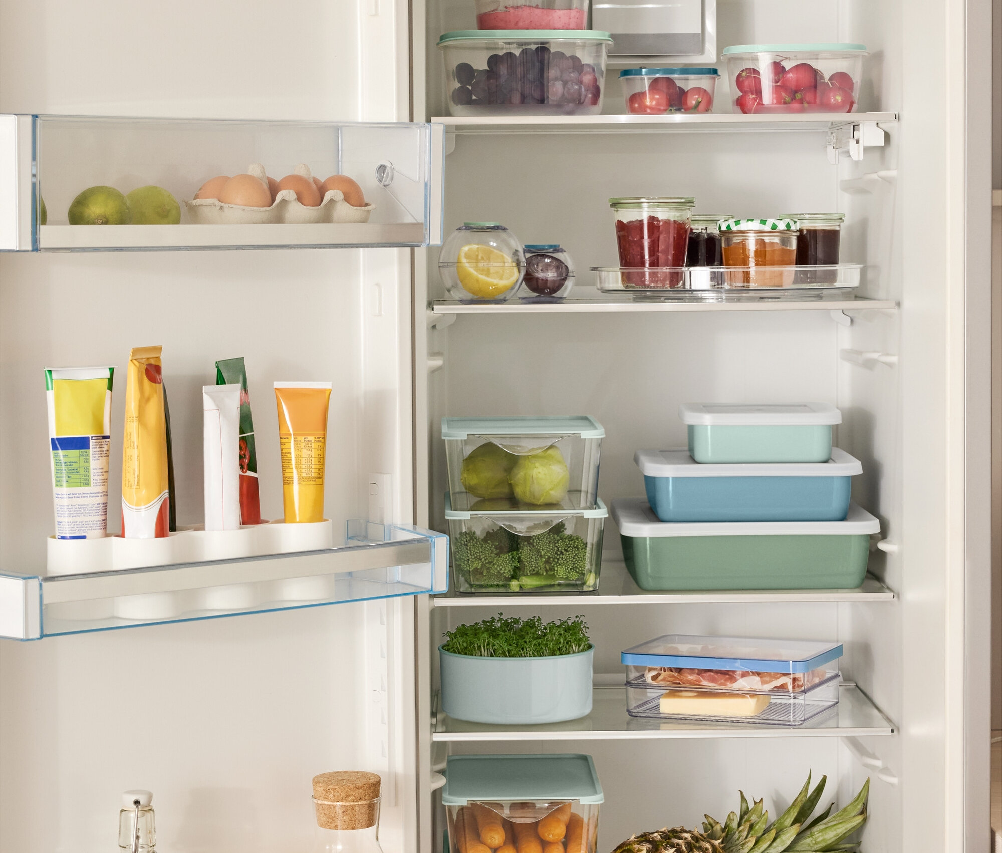 Otvorená chladnička plná rôznych potravín, vrátane 4 úložných boxov, 2 guľatých nádob na uchovávanie potravín, 3 smaltovaných zapekacích mís s vekom a otočného taniera.