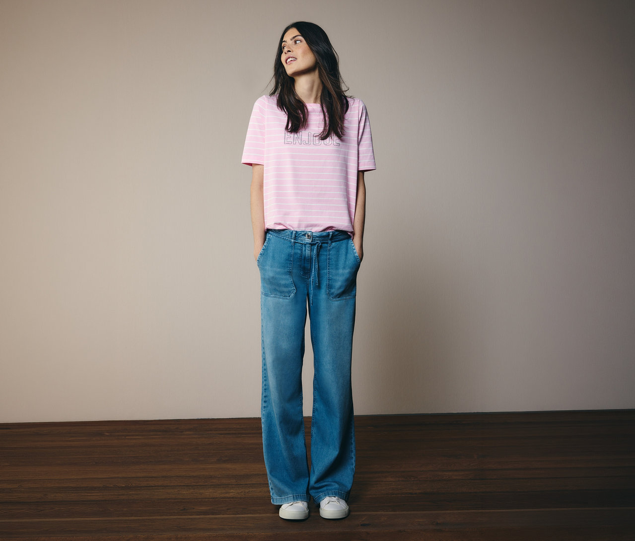 Žena s rukami vo vreckách nosí tričko CECIL s ružovými pruhmi a džínsy.