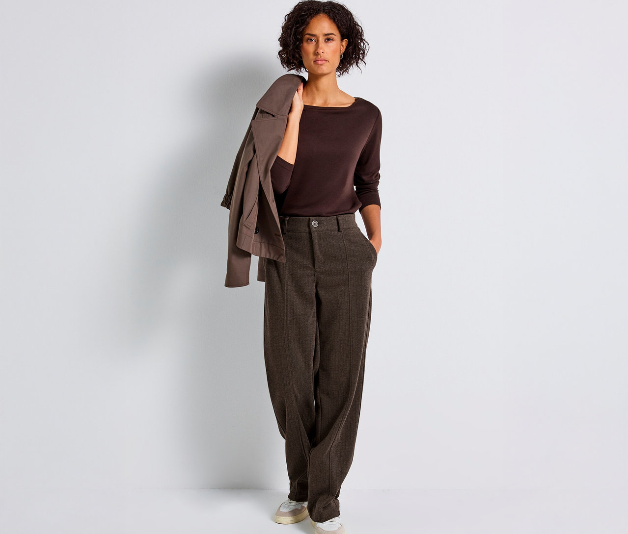 Žena stojí a má na sebe hnedé nohavice Street One Straight Leg, hnedý top a sako prehodené cez rameno.