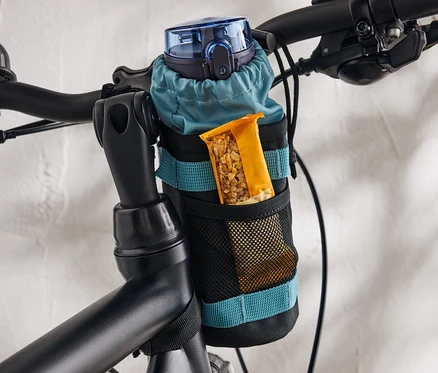 V držiaku pripevnenom na bicykli je modrá fľaša na vodu a müsli tyčinka.