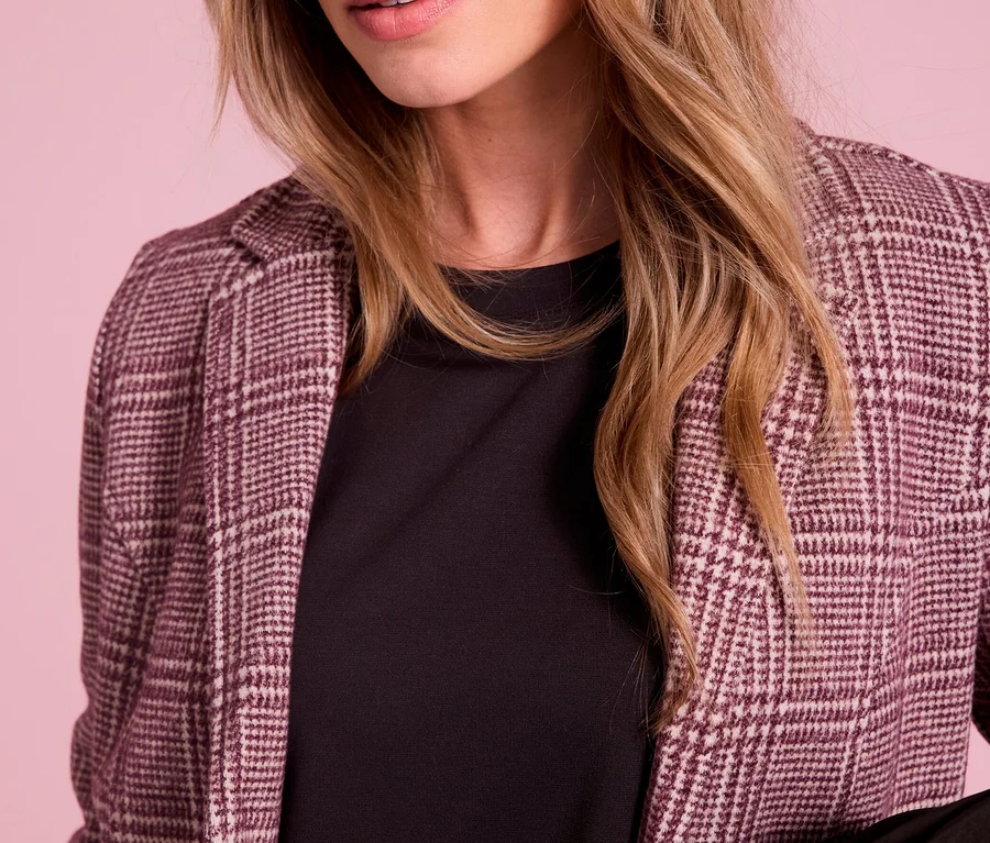 Detailný záber ženy s blond vlasmi a modrými očami, ktorá má na sebe károvaný blejzer Street One cez čierny top.