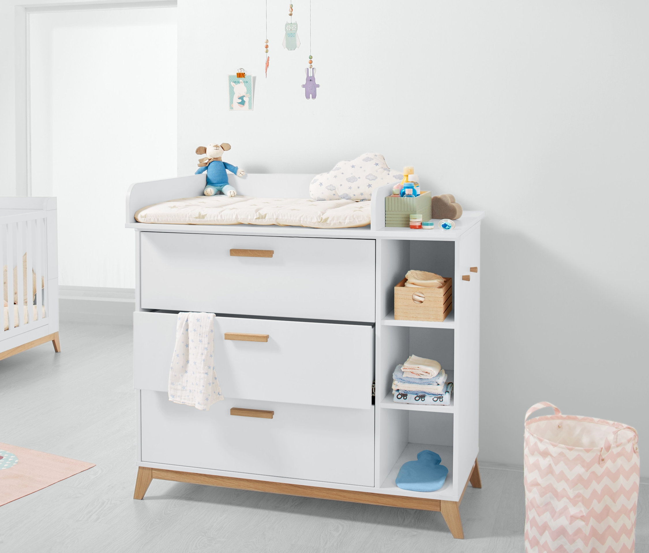 Biela komoda na prebaľovanie s tromi zásuvkami a otvorenými policami.