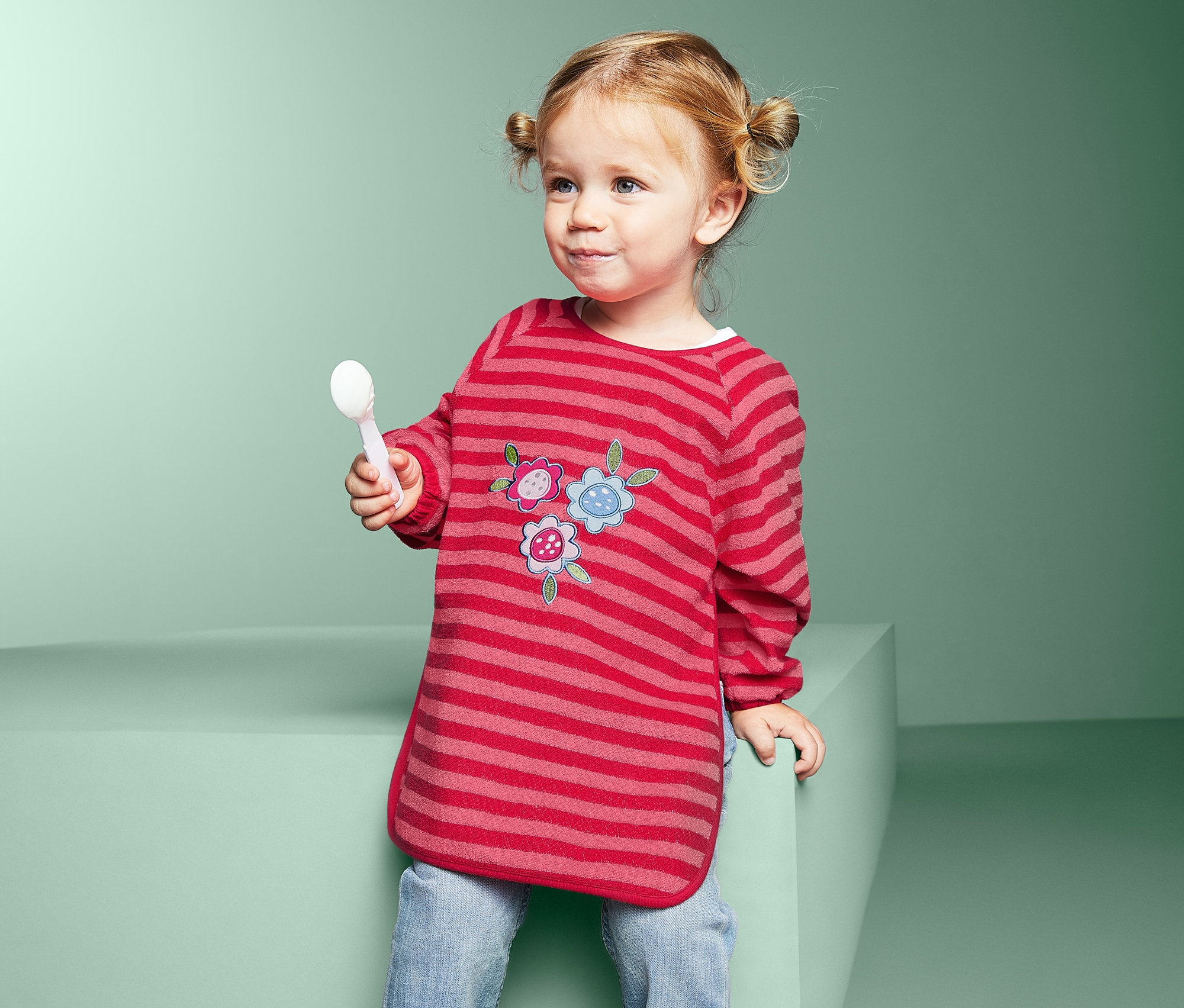 Dievčatko drží lyžicu a má na sebe podbradník s rukávmi, 2 ks.
