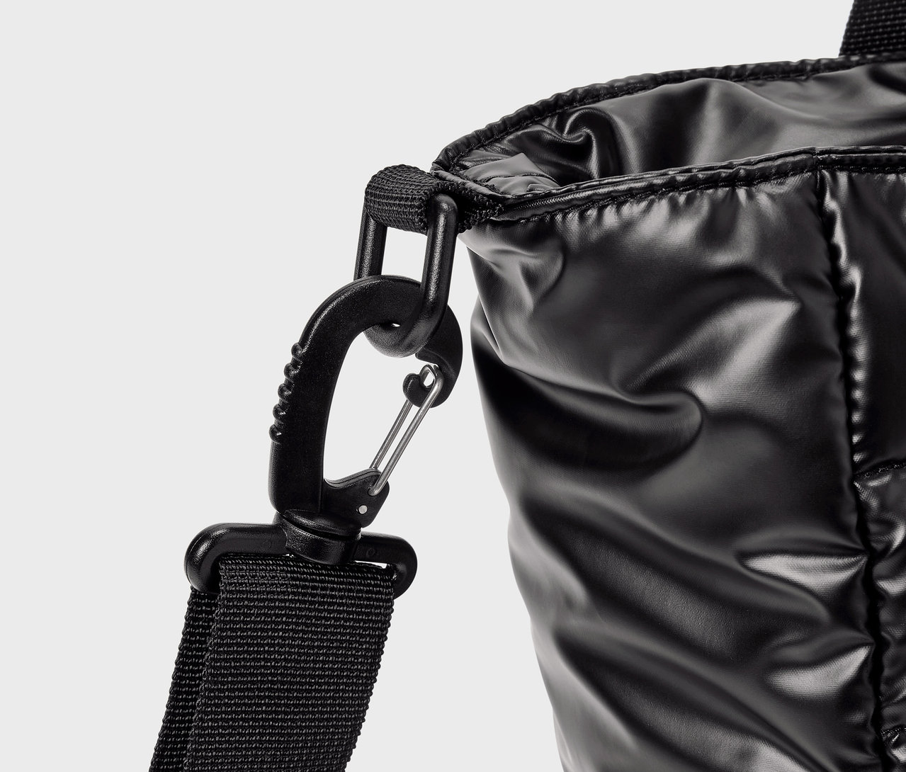 Detail lesklej čiernej tašky s karabínou.