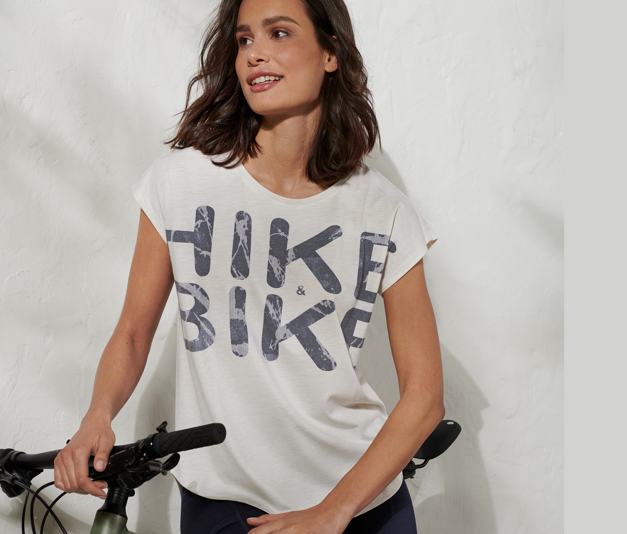 Žena opierajúca sa o bicykel má na sebe funkčné tričko s nápisom HIKE & BIKE.