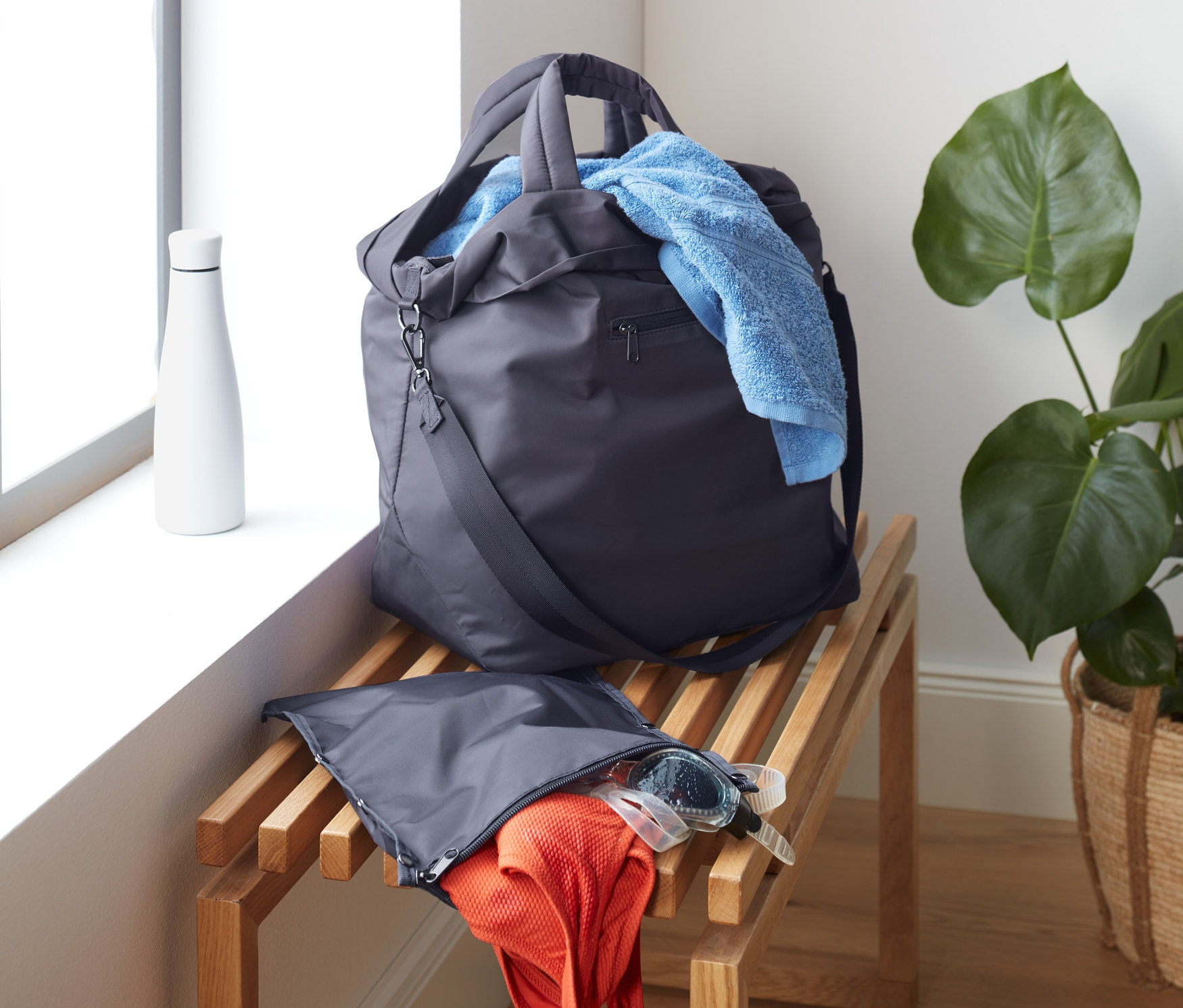 Športová taška leží na drevenej lavici vedľa okna. Z tašky vykúka modrý uterák.
