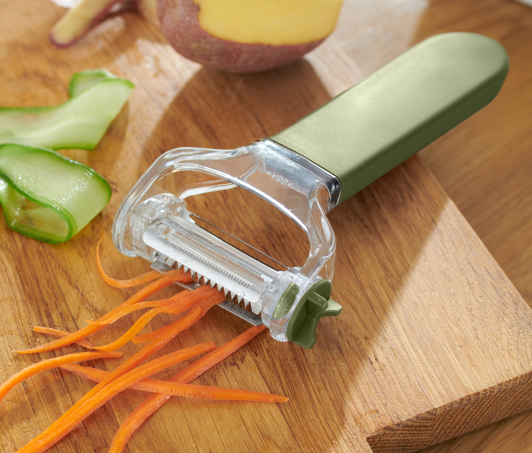 Univerzálna škrabka 3 v 1 na drevenej doske s mrkvou, uhorkou a zemiakom.