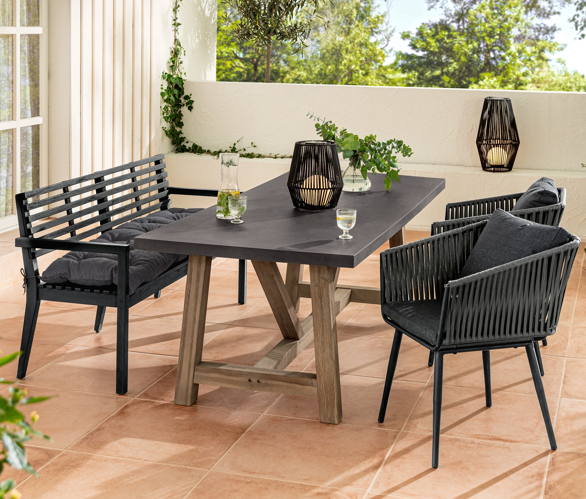 Záhradné sedenie so záhradnou lavicou s opierkami rúk a podložkou Sun Garden, jedálenským stolom s doskou z polycementu, jedálenskými kreslami s textilným výpletom a solárnym lampášom.