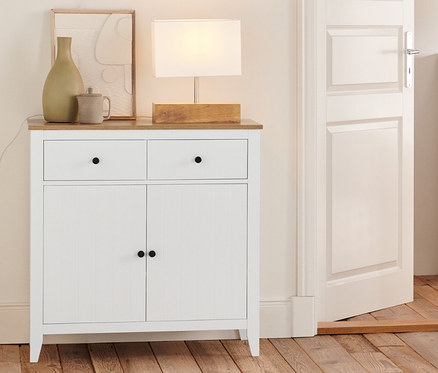 V izbe stojí komoda so zásuvkami, odkladacia skrinka, regál a stolová lampa s dreveným podstavcom.