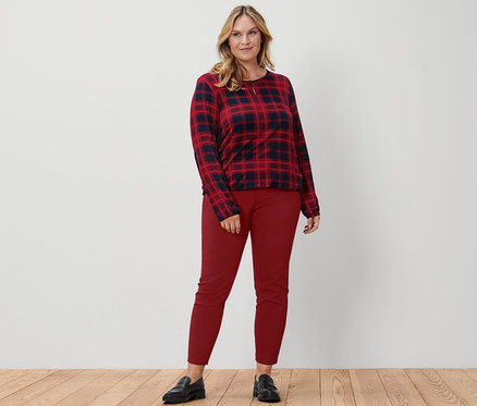 Žena stojí a má na sebe kárované blúzkové tričko, červené elastické nohavice a kožené mokasíny.