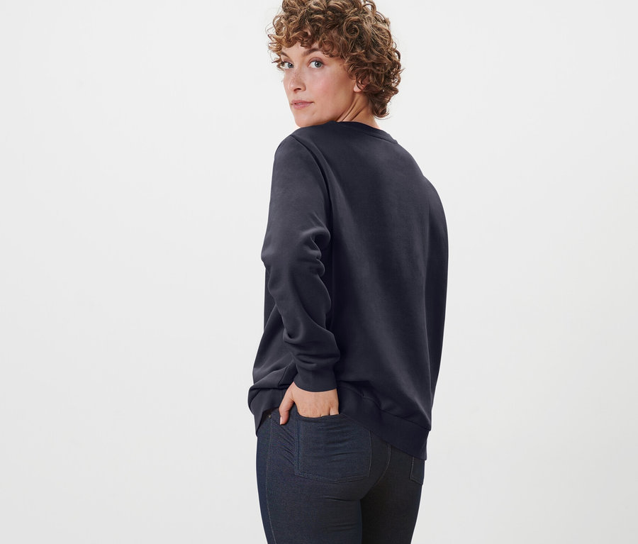 Žena sa pozerá cez rameno a pózuje v tmavomodrej mikine.