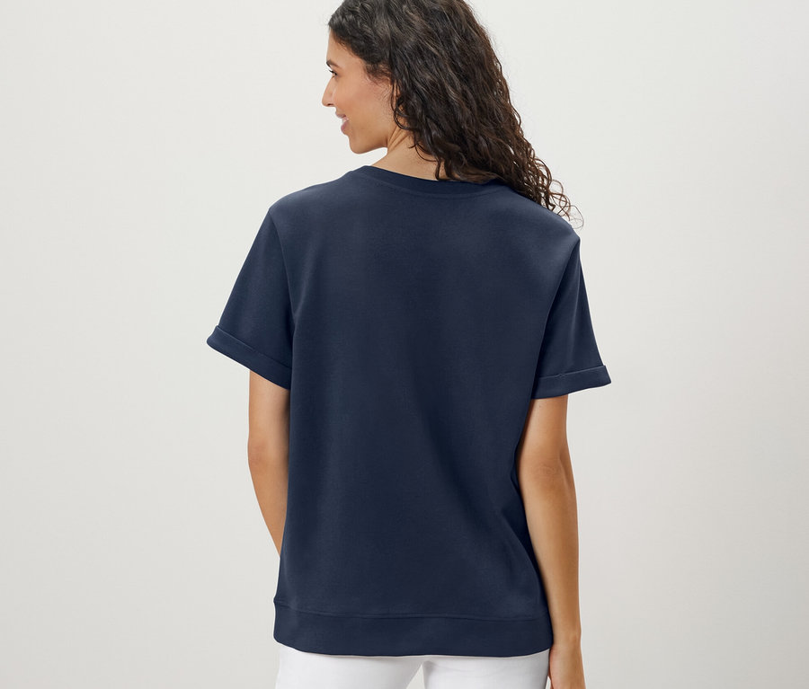 Pohľad zozadu na ženu s vlnitými vlasmi, ktorá má na sebe tmavomodré tričko zo zmesi modalu a biele nohavice.