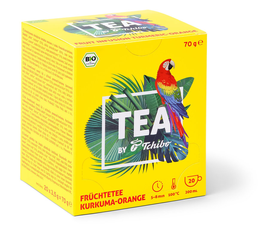 Žltá krabička čaju TEA by Tchibo BIO ovocný čaj s príchuťou kurkumy a pomaranča s obrázkom papagája a tropických listov.