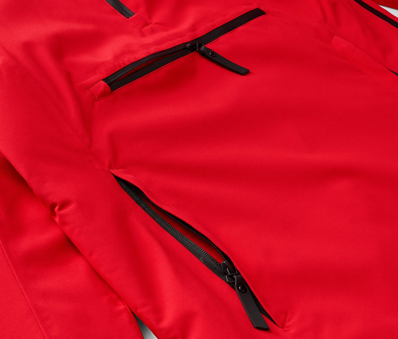 Detail červenej bundy s čiernymi zipsami na vreckách.