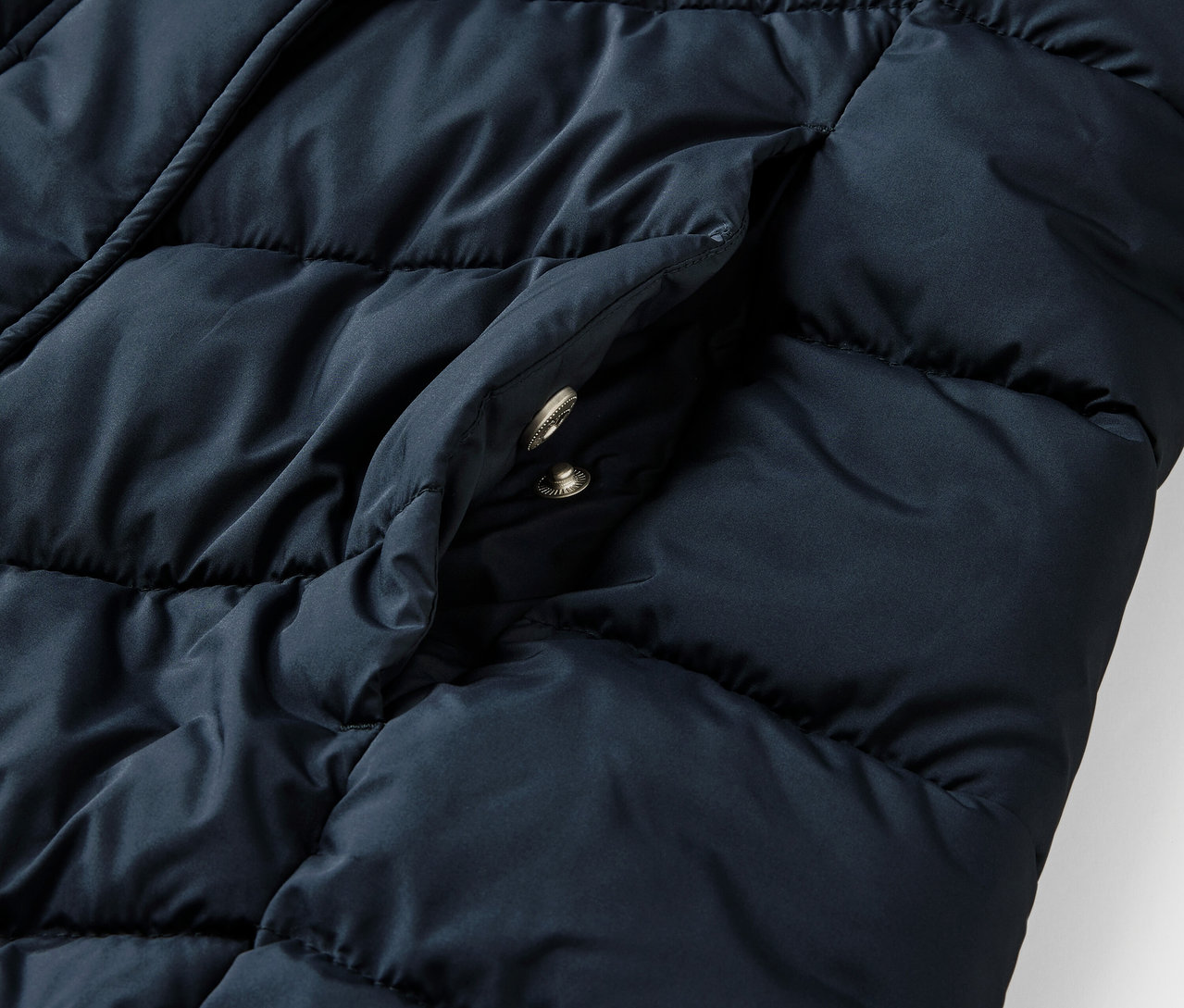 Detailný záber na tmavomodrú prešívanú bundu s kapucňou a vreckom.