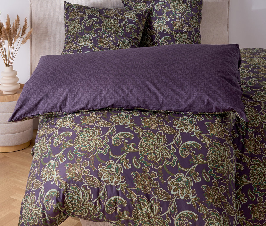 Posteľ s fialovou posteľnou bielizňou s kvetinovým vzorom a dvoma vankúšmi.