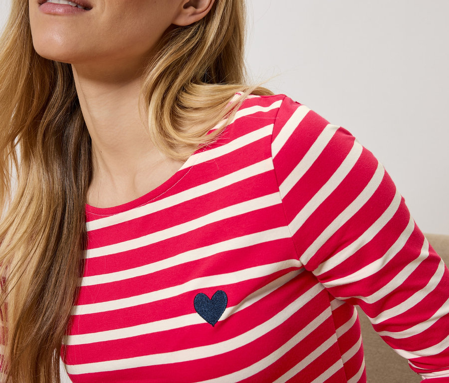 Blondínka má na sebe červeno-biele pruhované tričko s dlhým rukávom a tmavomodrým srdiečkom.