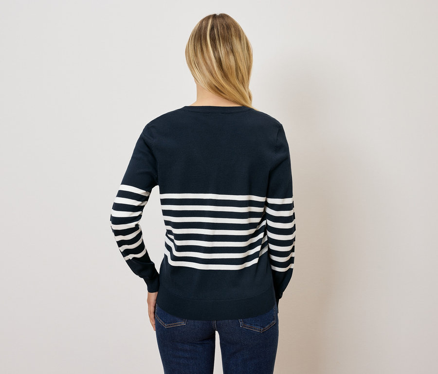 Zozadu je vidieť žena s blond vlasmi v modro-bielom prúžkovanom svetri a džínsoch.