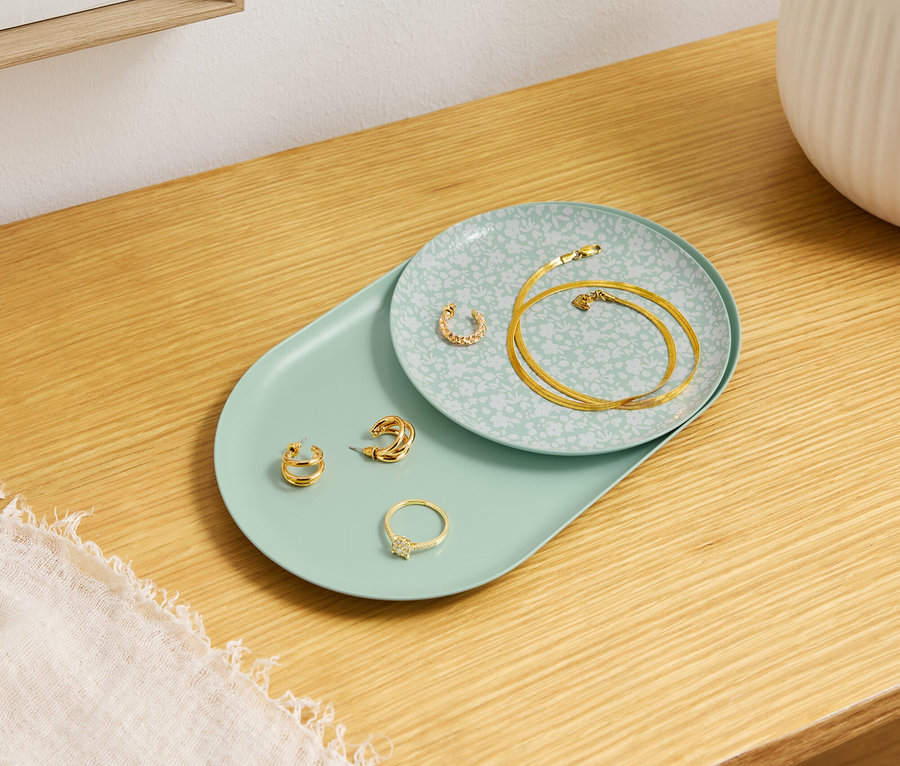 Zlaté šperky ležia na ozdobných tanieroch na drevenom stole.